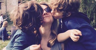 A mother of boys being kissed on the cheek by her sons