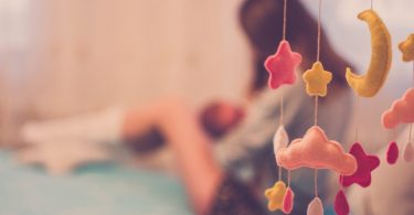 Baby sleep training: A mother sitting on a bed cuddling her baby