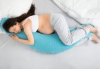 Pregnant woman lying on bed cuddilng sleep pillow