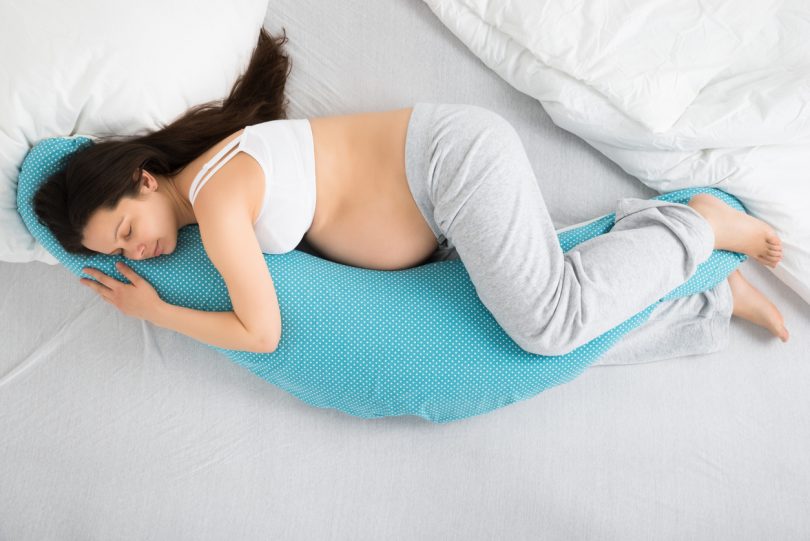 Pregnant woman lying on bed cuddilng sleep pillow